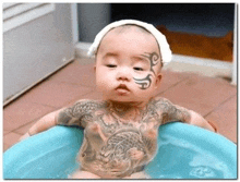 a baby with a lot of tattoos on his body is sitting in a tub of water .