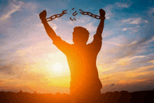 a silhouette of a man breaking chains at sunset .