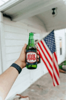 a person is holding a bottle of ales beer in front of an american flag