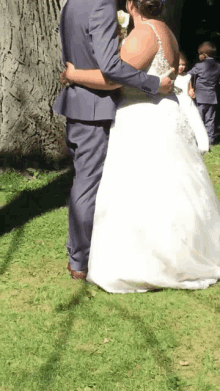 a bride and groom are hugging in the grass with a tree in the background