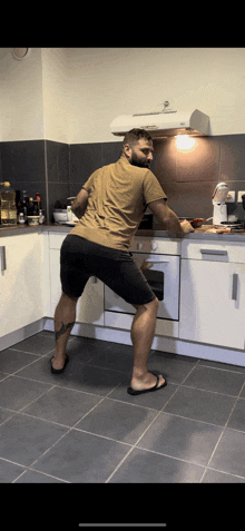 a man in a tan shirt is standing in a kitchen