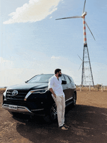 a man leans against a black toyota car in front of a windmill