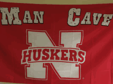 a red banner that says man cave huskers is hanging on a wall