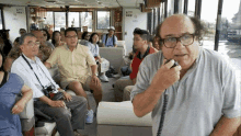 a man with glasses is talking into a walkie talkie in front of a group of people on a boat