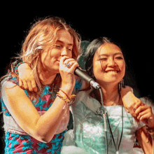 two women singing into microphones with one wearing a ring