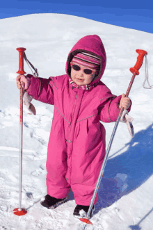 a little girl in a pink ski suit holds ski poles