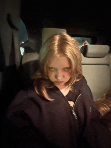 a young girl sitting in the back seat of a car making a face