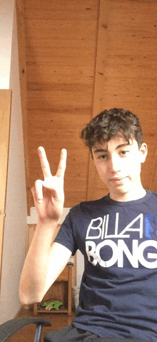 a young man wearing a blue billabong shirt giving a peace sign