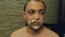 a shirtless man with a shaving cream on his face is looking at the camera .