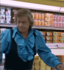 a man in a blue ruffled shirt is standing in front of a grocery aisle filled with cans of orange juice