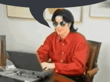 a man wearing sunglasses and a red shirt is typing on a laptop computer