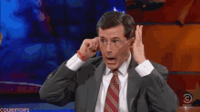 a man in a suit and tie is making a funny face in front of a screen that says colbert gifs