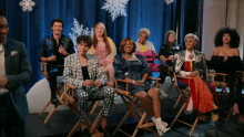 a group of people are sitting in director 's chairs in front of a blue curtain with snowflakes on it