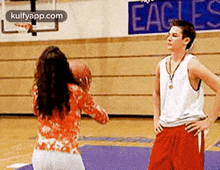 a man and a woman are playing basketball on a court with a sign that says eagles in the background .