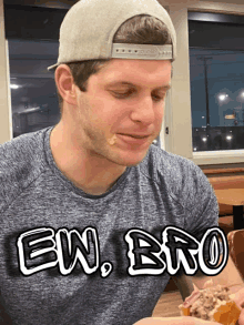 a man wearing a hat and a shirt that says ew bro eating a sandwich