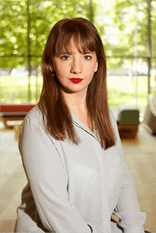 a woman in a light blue shirt with red lipstick stands in front of a window