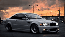 a silver bmw is parked in a parking lot with a sunset in the background