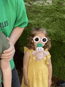 a little girl wearing sunglasses is holding a stuffed animal