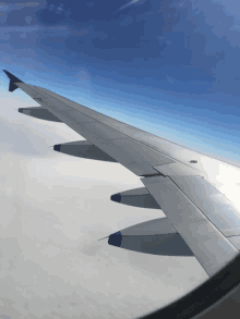 the wing of an airplane flying in the sky with a blue sky in the background