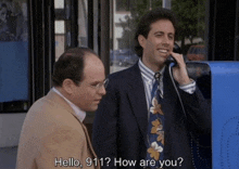 a man in a suit and tie talks on a pay phone while another man looks on