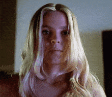 a woman with long blonde hair looks at the camera with a serious look on her face