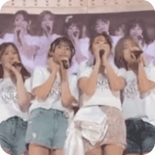 a group of girls are singing into microphones with their shirts saying akb on them