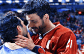 a man in a red jersey with the number 1 on the front kisses another man