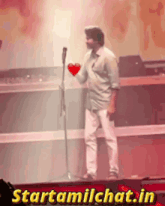 a man is holding a heart in front of a microphone and the website starttamilchat.in is behind him