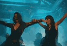 two women are dancing with their arms in the air in a dark room .