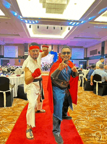 two men dressed in costumes are posing for a picture on a red carpet in a large room .