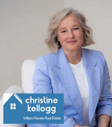 a woman in a blue jacket sits in front of a sign that says christine kellogg