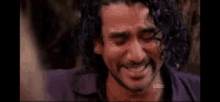 a man with curly hair is crying while wearing a purple shirt and smiling .