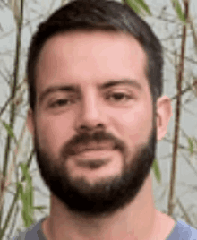 a man with a beard is smiling for the camera in front of a bamboo plant .