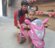 a little girl is pushing a little boy on a pink toy motorcycle