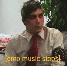 a man in a white shirt and red tie is sitting on a couch and says `` emo music stops '' .