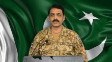 a man in a military uniform is standing at a podium with a microphone in front of a flag .