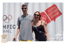 a man and a woman are posing for a picture in front of a sign that says youth olympic games