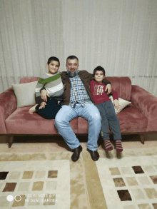 a man sits on a couch with two boys one of whom is wearing a shirt that says new york city