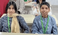 a boy and a girl are sitting at a desk in a classroom with other students .