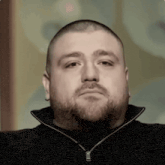 a man with a beard is wearing a black sweater and looking at the camera .