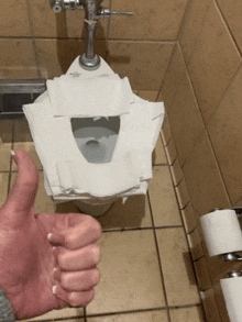 a hand giving a thumbs up in front of a toilet