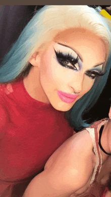 a drag queen with blue hair and pink lips is taking a selfie