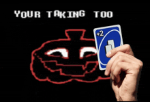 a hand is holding a uno card with a face on it in front of a screen that says your taking too