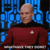 a bald man in a red shirt is sitting in front of a blue wall and asking what have they done .