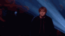 a man in a black jacket stands in front of a blue light