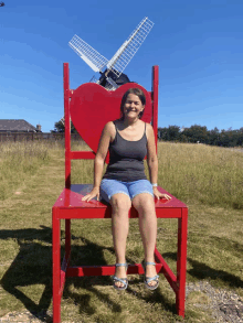 a woman sits on a large red chair with a heart on it in front of a windmill