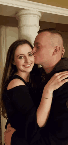 a man kisses a woman on the cheek in front of a white pillar