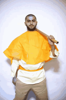 a man wearing an orange cape holds a bamboo stick over his shoulder