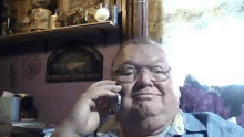 a man wearing glasses is talking on a cell phone while sitting in a chair .