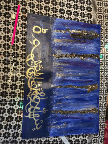 a blue and gold painting with arabic writing on it sits on a table